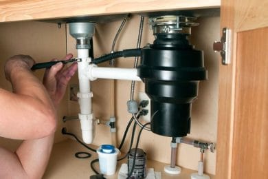 Plumber repairing a garbage disposal beneath a kitchen sink in Monroeville