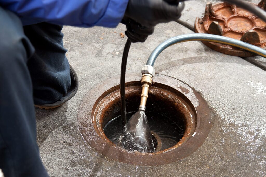 Plumber hydro jetting a sewer line through a manhole in Monroeville